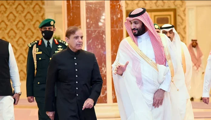 Saudi Crown Prince Mohammed bin Salman walking and talking with Pakistani Prime Minister Shehbaz Sharif during a formal visit, accompanied by officials and security personnel.